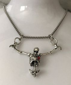 Embrace the darker side of fashion with our Hanging Skeleton Torso Necklace on a stainless steel 18" chain. This unique piece features a silver skeleton hanging from both wrists, adding a touch of Gothic flair to any outfit. You have the option to personalize your necklace by choosing between a skeleton with or without a striking red rhinestone heart accent. The skeleton's head is elegantly tilted forward, enhancing its macabre charm. Perfect for Halloween or as a statement accessory, this necklace comes beautifully presented in a sleek black gift box, making it an ideal gift for those who appreciate edgy and distinctive jewelry pieces. Punk Alloy Jewelry For Halloween, Emo Heart Pendant Metal Necklaces, Punk Style Metal Heart Pendant Necklace, Emo Heart Pendant Metal Necklace, Punk Style Metal Necklace With Heart Pendant, Gothic Stainless Steel Silver Chain Jewelry, Punk Stainless Steel Pendant Jewelry, Punk Style Necklace For Halloween Gift, Gothic Stainless Steel Clavicle Chain Necklace