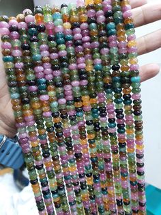 a person holding up some beads in their hand and the beading is multicolored