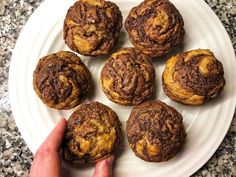 a person holding a plate full of chocolate muffins on a marble counter top