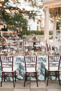 the tables are set with white chairs and floral tablecloths for an outdoor reception