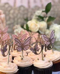 there are cupcakes with butterflies on top of them and some flowers in the background