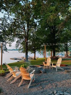 a fire pit surrounded by wooden chairs in the middle of a gravel area next to trees