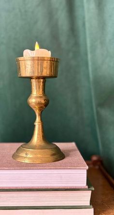 a gold candle holder sitting on top of two pink books in front of a green curtain