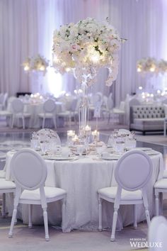 an elegant wedding reception with white flowers and candles in the centerpieces on round tables