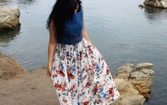 a woman is standing by the water wearing a dress and holding an umbrella in her hand