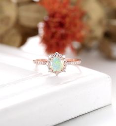 an opal and diamond ring sitting on top of a white box next to flowers