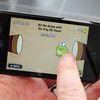 a person holding a cell phone in their left hand and pointing to the screen with an animated frog on it