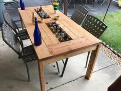 a wooden table with bottles and glasses on it sitting in the middle of a patio