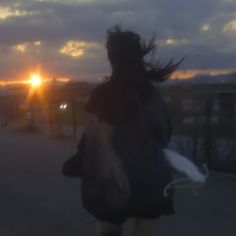 a blurry image of a woman walking down the street at sunset with her hair blowing in the wind