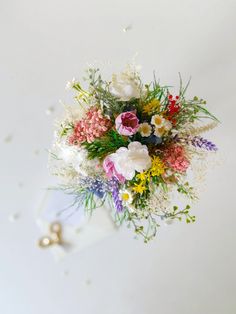 a bouquet of flowers sitting on top of a white table next to a gold ring