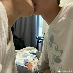 a man and woman kissing each other in front of a bed with a mickey mouse shirt on