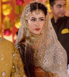 a woman in a bridal outfit is looking at the camera while another man stands behind her