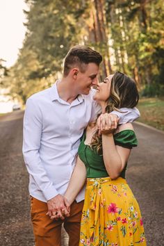 a young man and woman are kissing on the street in front of some tall trees