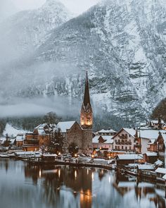 an old church in the middle of a lake surrounded by snow covered mountains and houses