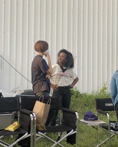 three people sitting in lawn chairs with bags on their backs and one person standing next to them