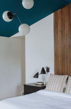 a white bed sitting in a bedroom next to a wall mounted lamp and wooden headboard