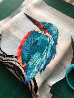 a piece of fabric with a bird painted on it and scissors next to it sitting on a cutting board