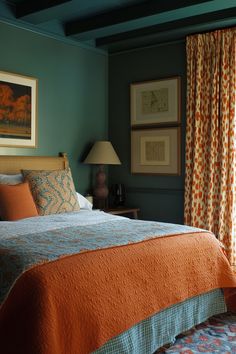 a bed sitting in a bedroom next to a window covered in orange and blue curtains