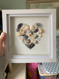 a heart made out of seashells in a white frame on top of a table