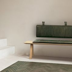 a green leather bench sitting on top of a wooden table next to a white wall