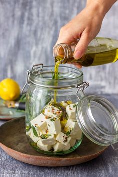 someone pouring olive oil over tofu cubes in a glass jar on a plate