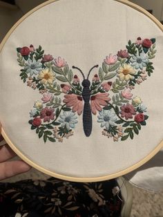 a hand embroidered butterfly with flowers and leaves on it's wings is held up in front of the camera