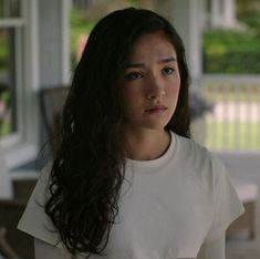 a woman with long dark hair wearing a white t - shirt looking at the camera