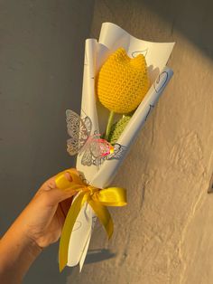 a person holding a yellow flower in a white paper wrapper with butterflies on it