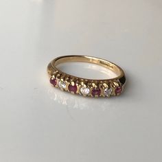 A Vintage 9 carat gold Ruby and diamond ring. This beautiful piece holds all seven stones neatly in line, with a diamond in between each glowing ruby. The settings hold each stone neatly while displaying all the sparkle from them. CONDITION: Wear consistent with age and use. Please see photos for more detail. ASSAYED IN BIRMINGHAM CIRCA 1989 SETTING (ACROSS): 21mm SETTING WIDTH: 3.5mm RUBY DIAMETER: 2mm DIAMOND DIAMETER: 2mm BAND WIDTH (SMALLEST): 2mm RING SIZE: UK: N | US: 6 1/2 WEIGHT: 2.4 grams (UZZ) Classic Yellow Gold Ruby Ring With Single Cut Diamonds, Formal Ruby Ring With Single Cut Diamonds, Formal Ruby Diamond Ring With Single Cut Diamonds, Classic Half Eternity Ruby Ring, Classic Ruby Ring In Diamond White, Classic Half Eternity Ruby Ring Gift, Classic Ruby Half Eternity Ring As Gift, Classic Ruby Half Eternity Ring For Anniversary, Classic Red Diamond Ring With Single Cut Diamonds