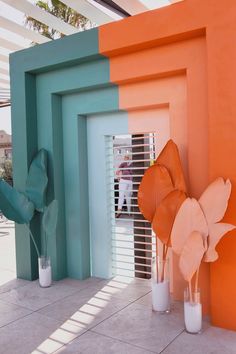 an orange and blue sculpture next to two vases with flowers in them on the side of a building