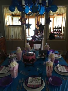 a birthday cake and cupcakes on a blue table cloth in front of a window