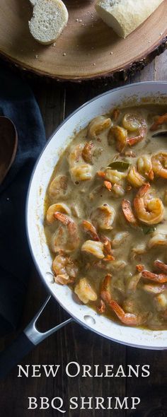 a bowl filled with shrimp and grits next to bread on a wooden table top