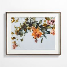 an orange flower is hanging on the wall in front of a white wall with a brown frame