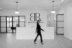 a black and white photo of a woman walking in front of a beauty by design sign