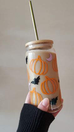 a hand holding a cup with a straw in it that has pumpkins and bats on it