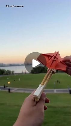 someone is holding a red and white paper airplane in front of a lake with people on it