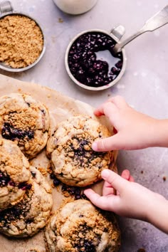 a person holding a cookie in front of some blueberry muffins on a table