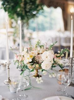 a table topped with lots of white flowers next to tall silver candlesticks and plates