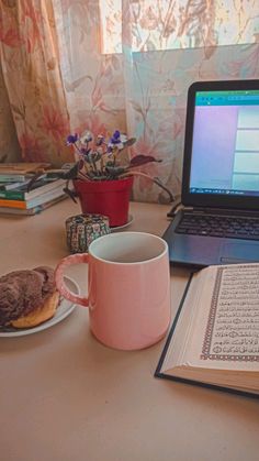 a laptop computer sitting on top of a desk next to a cup of coffee and donut