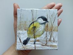 a painting of a bird sitting on top of a piece of white paper in someone's hand