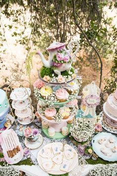 a table topped with lots of cakes and cupcakes next to a tea pot