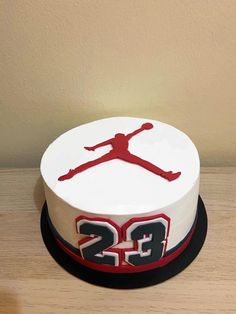 a white and red cake with the number 25 on it's side, sitting on top of a wooden table