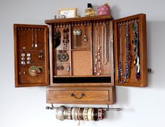 a wooden jewelry cabinet filled with lots of necklaces and bracelets hanging from it's sides