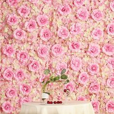 a table topped with a vase filled with flowers next to a wall covered in pink roses