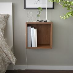 a wooden shelf with books and glasses on it next to a plant in a vase