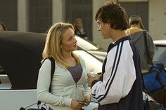 a man and woman talking to each other in front of parked cars on the street