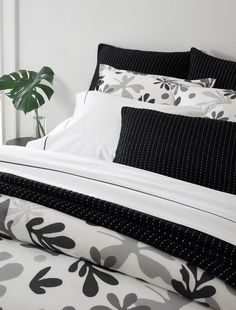 a bed with black and white sheets, pillow cases and a plant in the corner