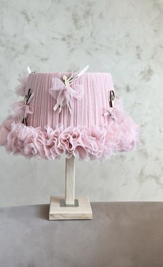 a pink lamp shade with ruffles and bows on the bottom is sitting on a table