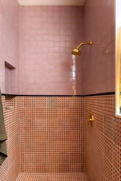 a pink tiled bathroom with gold fixtures and towels hanging on the shower headrests