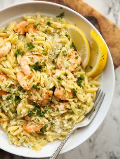 a white bowl filled with pasta and shrimp on top of a wooden cutting board next to a lemon wedge